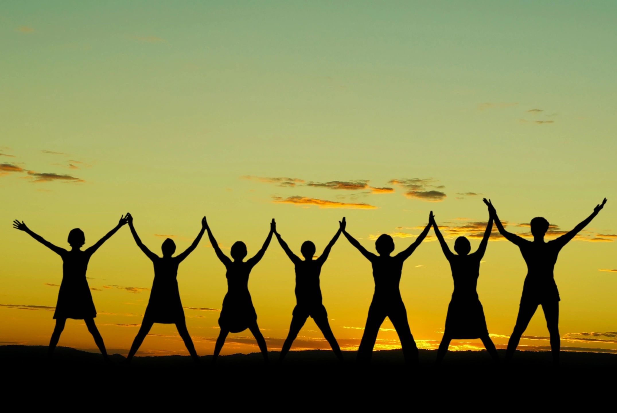 Silhouette of people with arms raised at sunset
